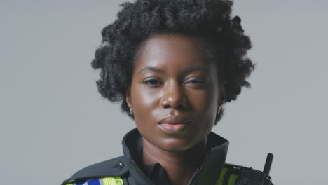 studio portrait of smiling young female police officer against plain background