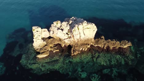 Aerial-flying-above-crystal-clear-turquoise-Sardinian-sea-water,-flying-forward-towards-white-rock-formation,-sunset