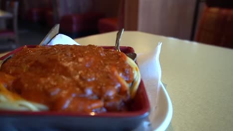 rotating-180-degree-semi-circle-tabletop-camera-closeup-of-plated-Italian-spaghetti-with-red-bolognese-beefy-sauce-spiced-herbed-with-a-spoon-and-fork-at-a-resturaunt-with-the-background-blurred