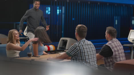 a joyful black african-american man runs up to friends giving five different ethnic groups of people sitting at a table in a bowling club. to celebrate and congratulate on the victory scored streak.