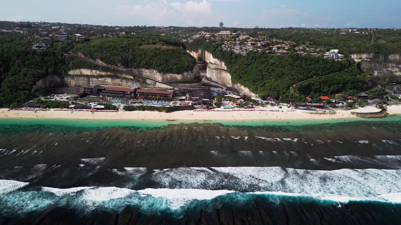 Aerial footage of Melasti Beach in Uluwatu featuring golden cliffs, turquoise ocean, and stylish beach clubs along pristine sand, capturing Bali’s coastal charm and dramatic seaside scenery