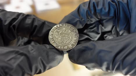 coleccionista examinando una moneda de plata portuguesa de la época medieval
