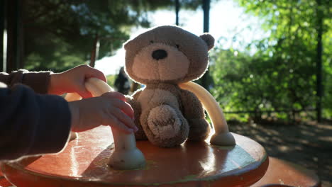 child playing with a teddy bear on a playground merry-go-round