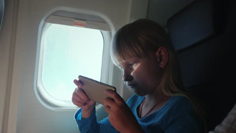 a blonde girl plays on a smartphone while flying in an airplane