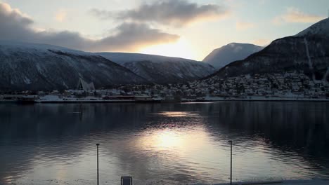 bella toma estática al atardecer de un mar con un pueblo nevado rodeado de montañas reflejadas en el agua