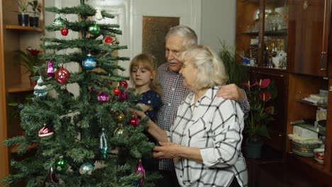 Kleines-Mädchen-Mit-Großmutter-Und-Großvater,-Die-Einen-Künstlichen-Weihnachtsbaum-Mit-Spielzeug-Dekorieren