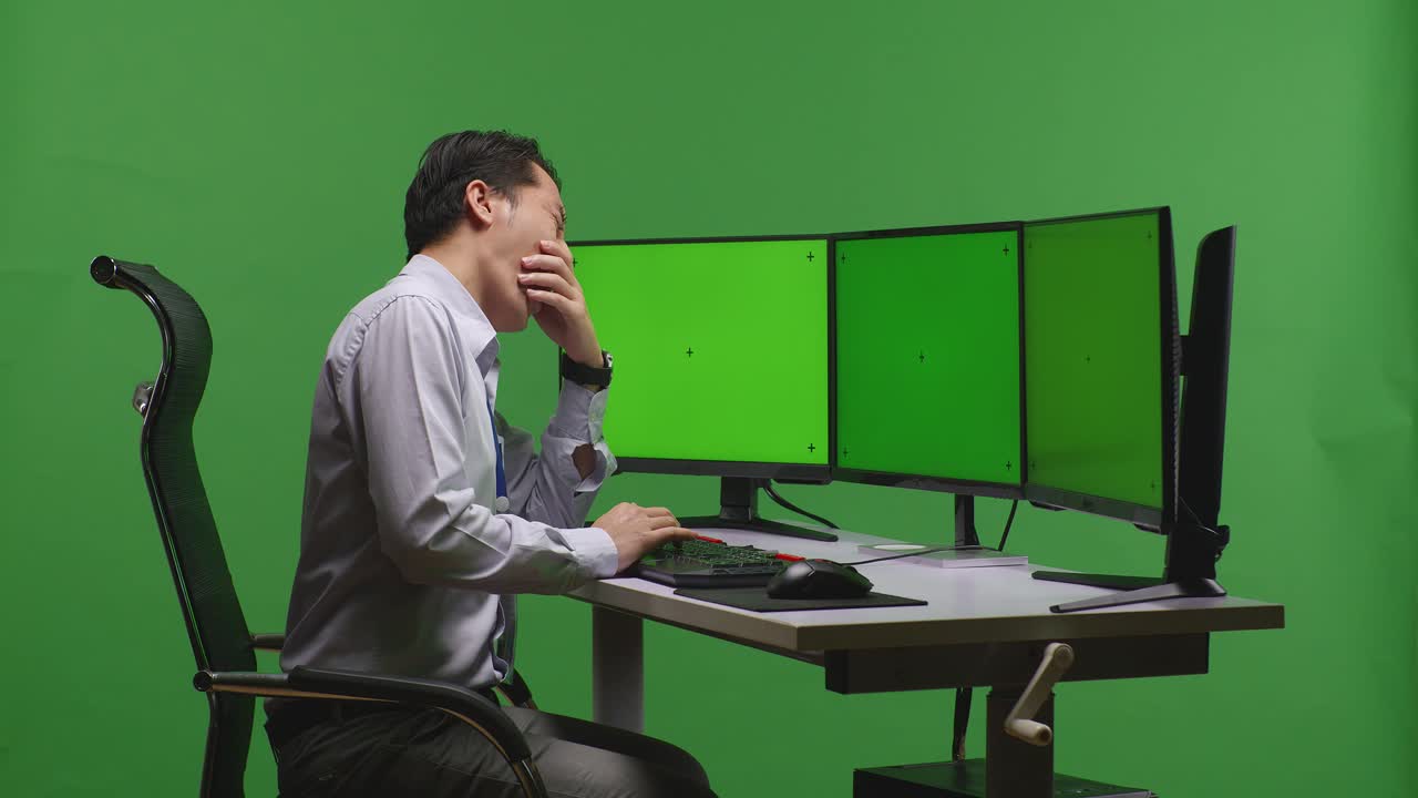 여러 개의 모니터를 가진 책상에 앉아있는 사람