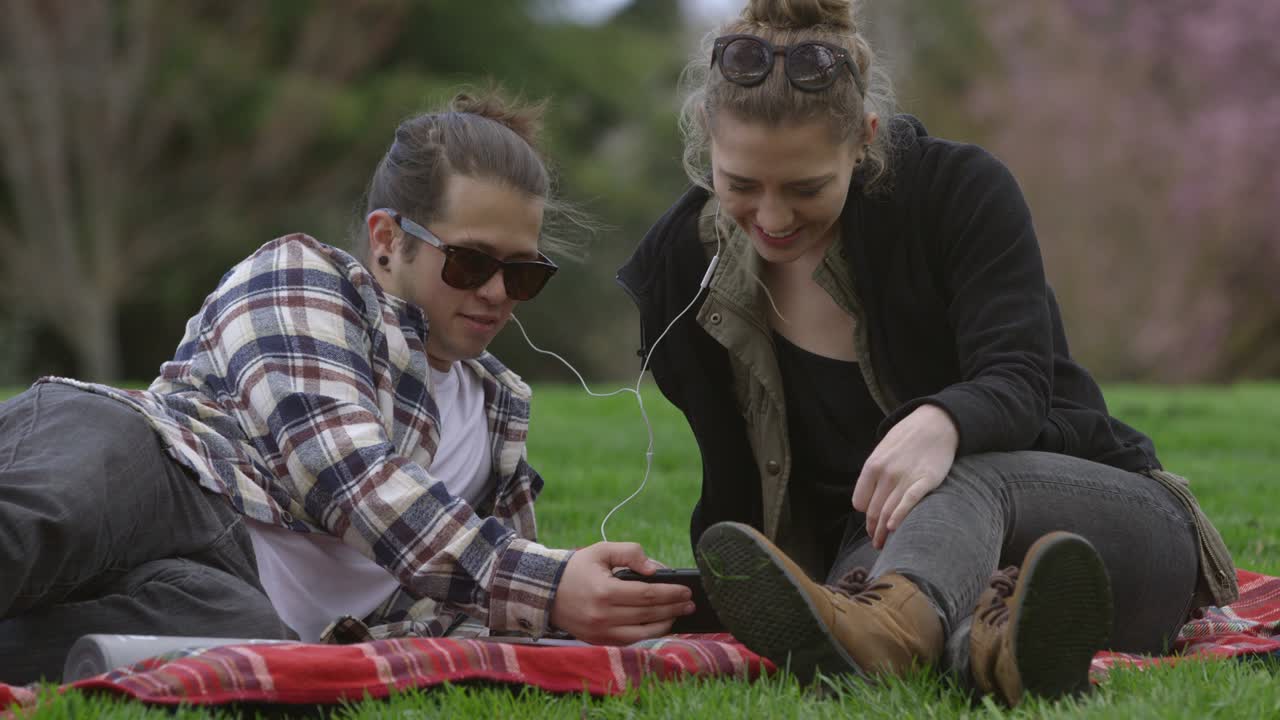 dos jóvenes en el parque en una manta escuchando música juntos