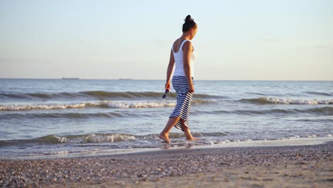 young female walking along the seashore. woman walks in the sea water of a sandy beach at sunset. summer vacation.