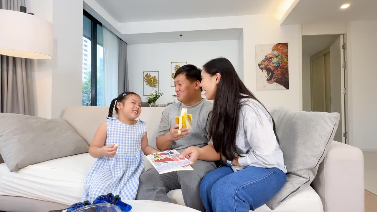 Family reading books and sharing fruit together on a cozy sofa in a modern home