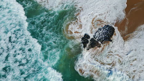 drone view powerful waves rolling on beautiful sandy beach with volcanic cliffs.