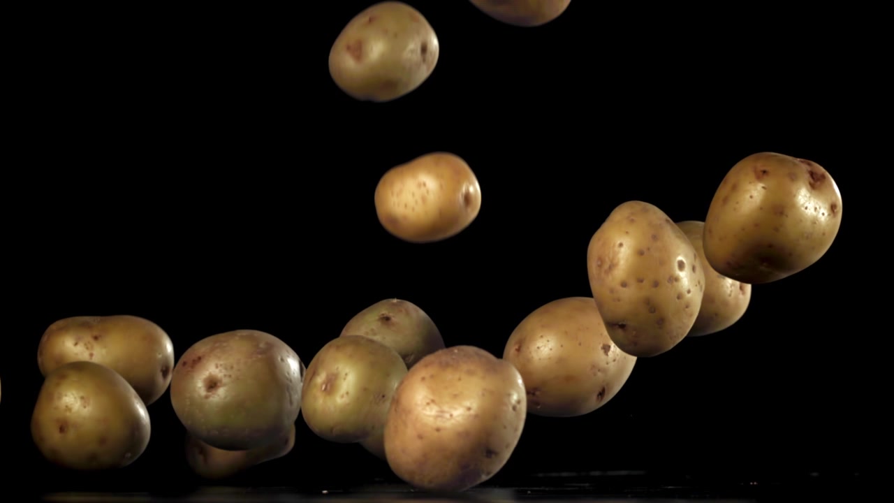 Patate fresche e crude che cadono al rallentatore su sfondo nero