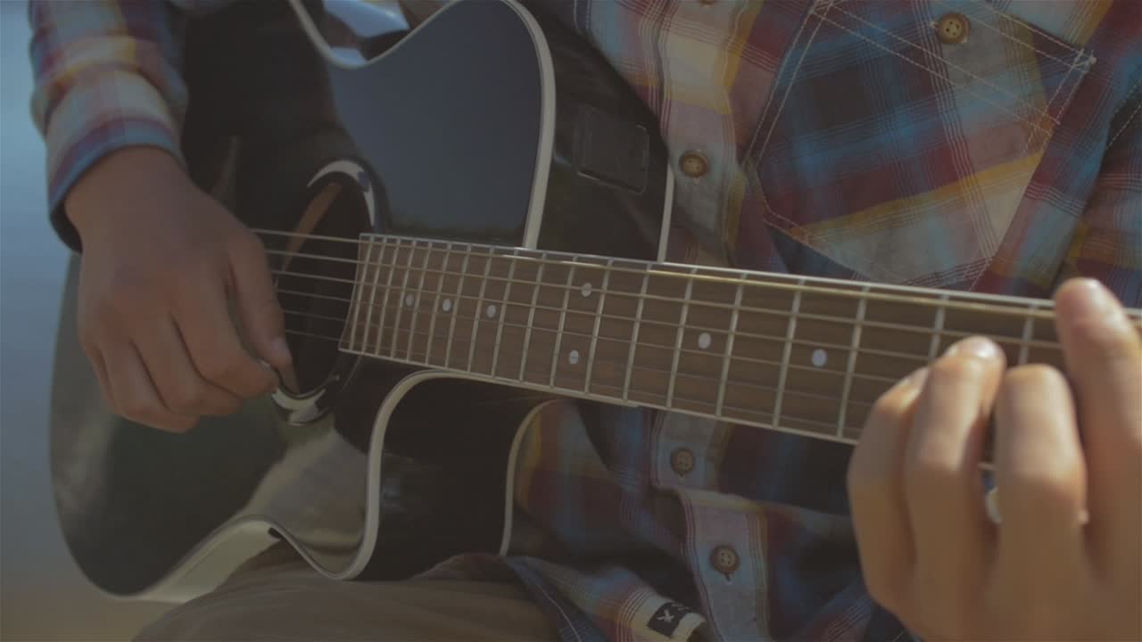 fotografía de cerca de un joven tocando música en su guitarra acústica en la orilla de un lago