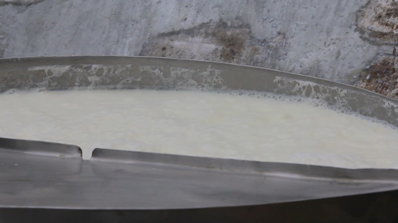 una vista de cerca del llenado de leche en un recipiente, haciendo espuma en la parte superior, una pared sucia en el fondo