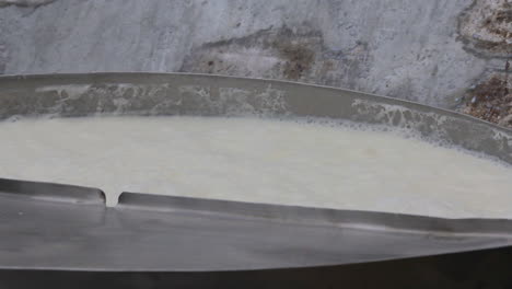 a close up view of milk filling in a container, making froth at the top, a dirty wall in the background