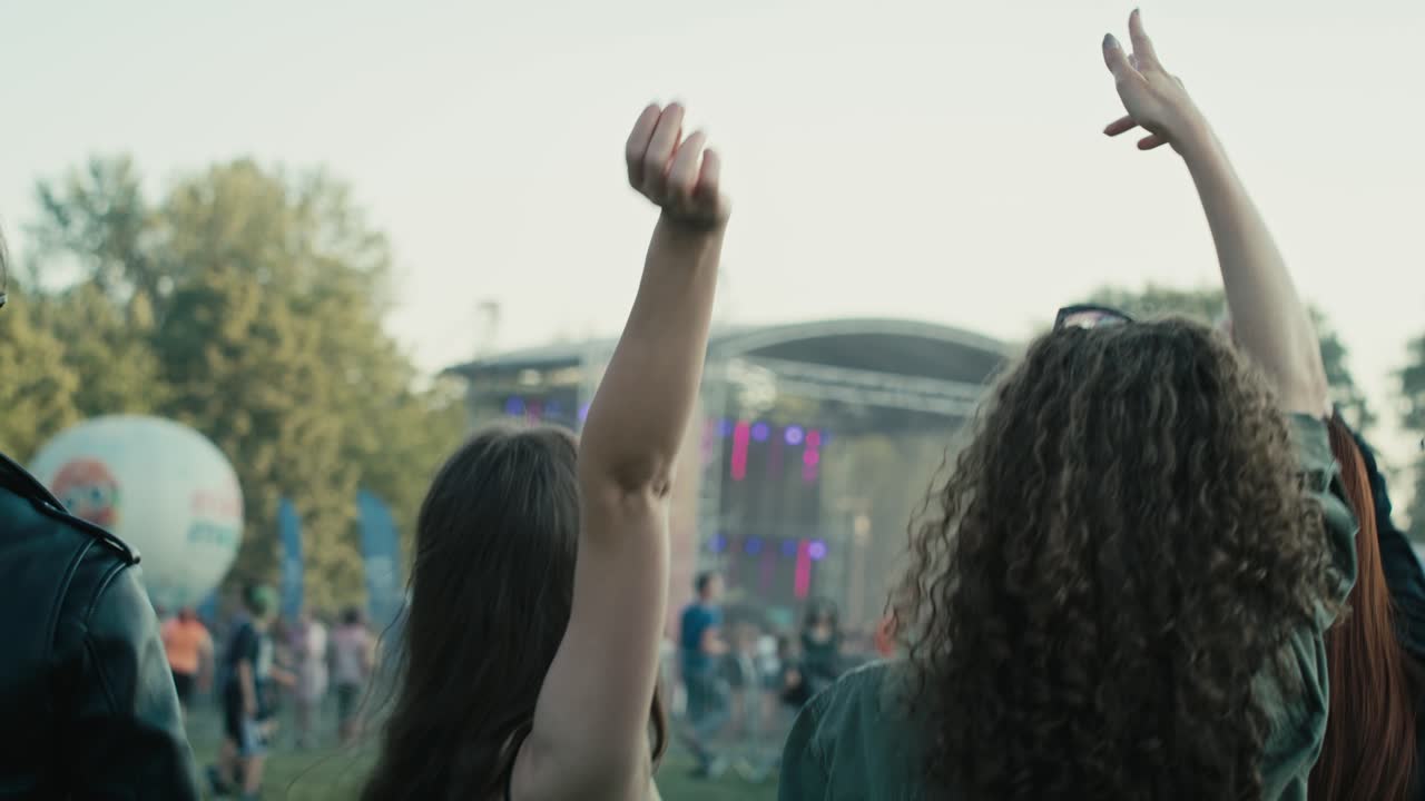 Venner danser på musikfestival med hænderne i vejret, set bagfra
