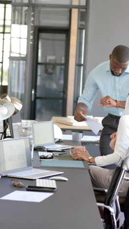 vertical video: business colleagues discussing documents and using laptops in modern office