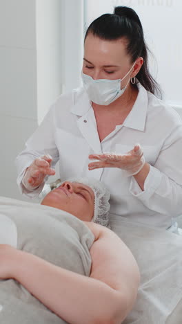 beautician applying moisturizing medical chemical peeling cream mask on young adult woman face