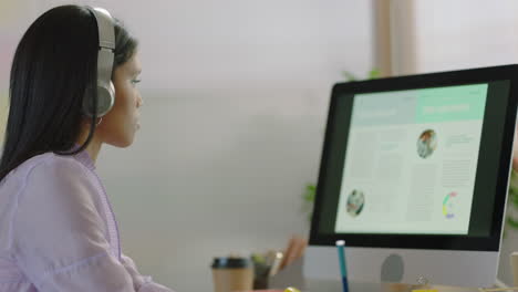 beautiful-young-mixed-race-woman-student-using-computer-graph-data-brainstorming-working-on-creative-project-enjoying-study-in-colorful-modern-office-listening-to-music-wearing-headphones