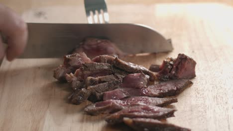 close slow motion slider shot of a medium rare steak being sliced with a chef knife and fork