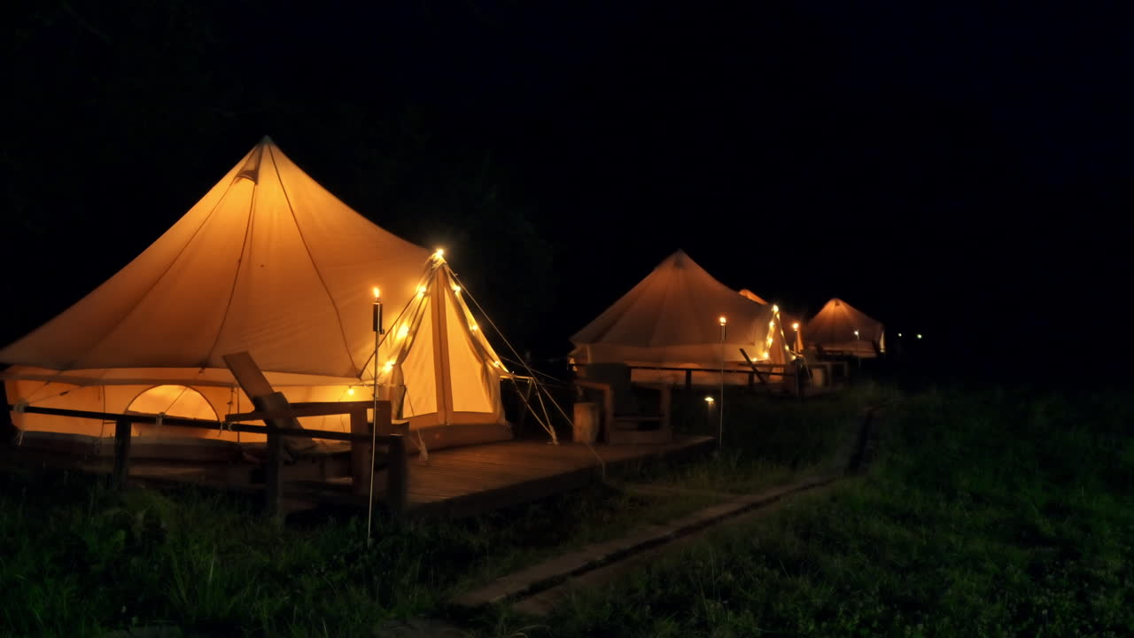 Telte med brændende fakler, lamper og træstole ved glamping om natten