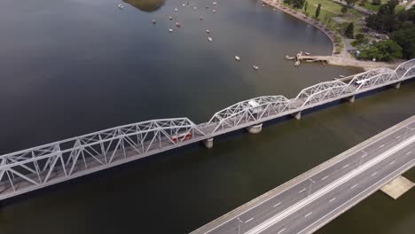 Aerial-view-of-Orange-bus-crossing-Barra-de-Santa-Lucia-Bridge-with-anchored-boats-below-in-the-river