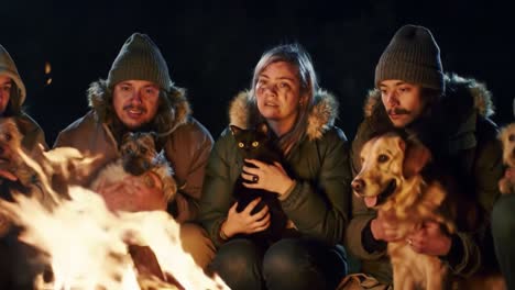 warm moments around the fire: a group of friends enjoying a cozy evening with their beloved dogs by a crackling campfire under a starry night sky