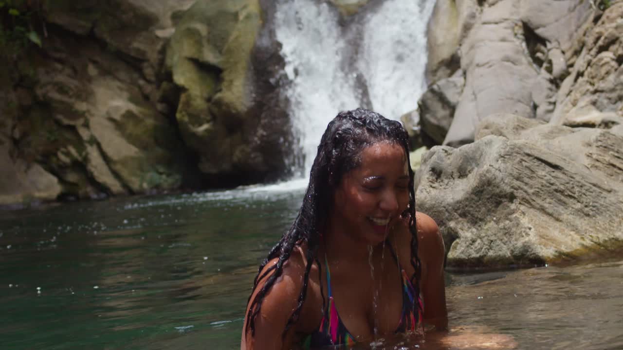 Uma jovem emerge da água de uma cascata no Caribe