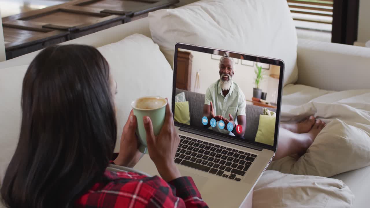 African american woman holding coffee cup having a video call on laptop sitting on the couch at home