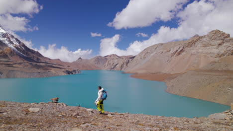 Female-tourists-trek-world's-highest-altitude-lake-at-Annapurna-Mountain-region-Nepal,-enjoying-walking-beside-the-Lake,-sunny-weather,-and-amazing-view-Drone-shot-4K