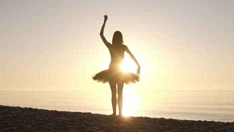 graceful young girl in ballet tutu standing on a coastline facing to the sea. waving her hands. doing ballet moves. sun shines. backside view