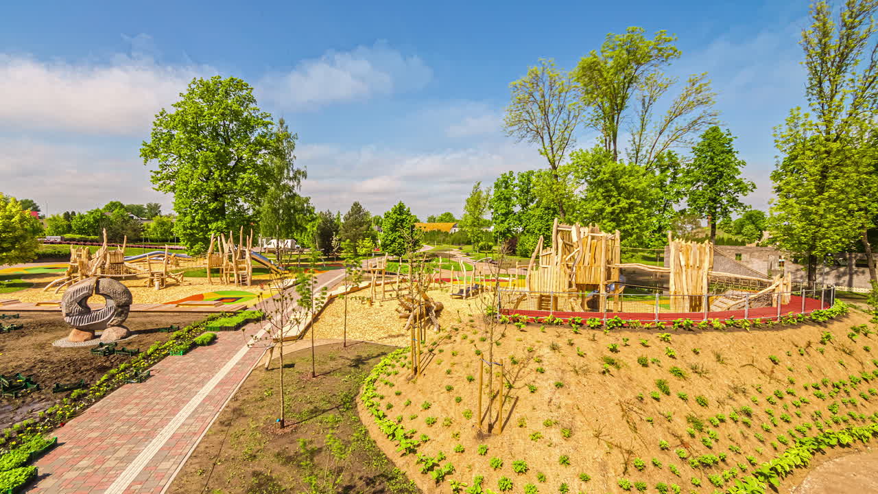 Overview of a playground on one side of a pathway and floral plants been planted in a beautiful garden in timelapse at daytime