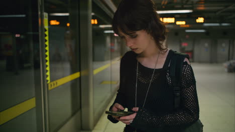 Aufnahme-Einer-Frau-Im-Alternativen-Stil,-Die-Auf-Dem-Bahnsteig-Einer-Londoner-U-Bahn-Wartet-Und-In-Echtzeit-Ihr-Mobiltelefon-Benutzt