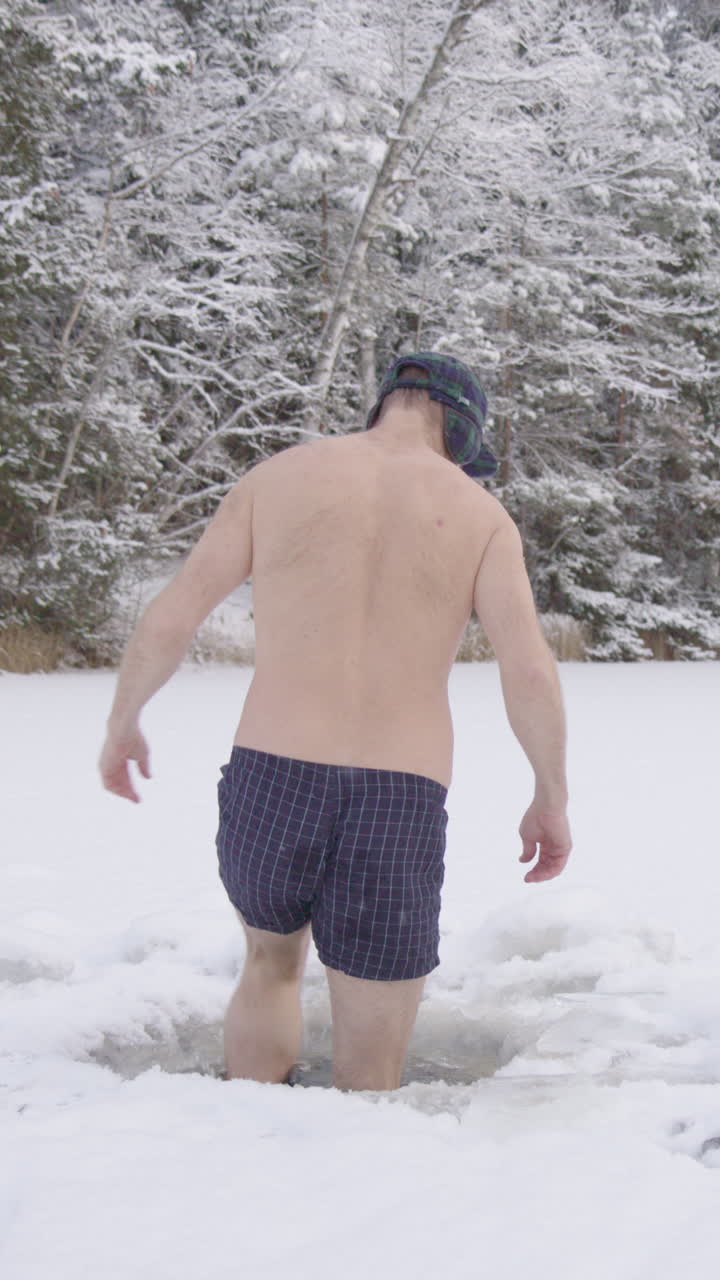 A crazy ice bathing man steps down into his ice hole in frozen lake, vertical