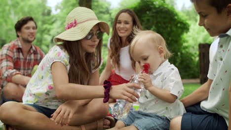 Familie-Sitzt-Auf-Einer-Decke-Im-Park.-Entzückendes-Kleinkind,-Das-Wasser-Aus-Der-Flasche-Trinkt