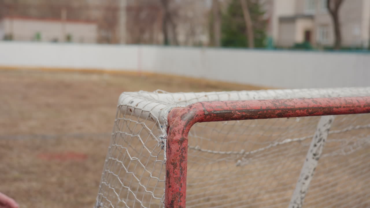 hands of caucasian player draping jacket over metal railing beside goal, puffy coat and cold field visible, practical gesture after play, casual pause on urban pitch with chain-link and chipped paint