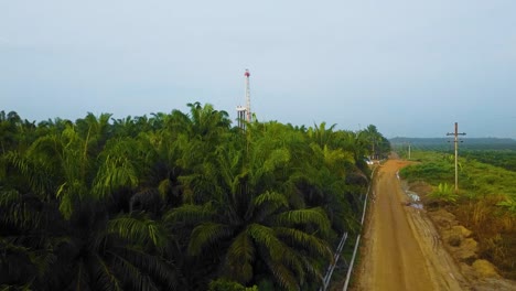 Cinematic-Drone-Shot-of-Onshore-Drilling-and-Workover-Rig-structure-and-Rig-equipment-for-oil-exploration-and-exploitation-in-the-middle-of-jungle-surrounded-by-palm-oil-trees-during-sunset-time