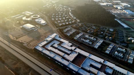 an expansive urban scene showing industrial buildings, residential housing, rail lines, roads, and surrounding infrastructure illuminated by warm evening light.