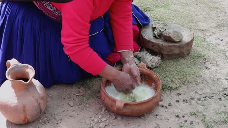 peruvian woman in traditional dress washes wool in bowl by hand