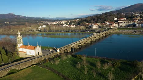 Kirchengebäude-Gegenüber-Der-Alten-Dorfstadt-Ponte-De-Lima,-Verbunden-Durch-Eine-Brücke,-Während-Ein-Vogelschwarm-Fliegt