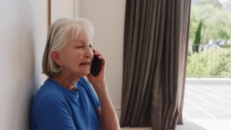 senior woman in blue shirt talking on smartphone at home, looking thoughtful
