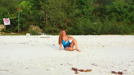feliz y atractiva mujer caucásica sonriendo en una playa de arena blanca relajándose frente a la luz del sol, fondo de plantas tropicales verdes