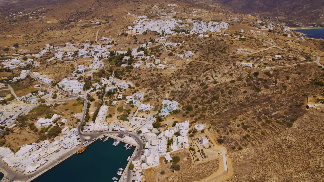 Aerial view of a picturesque Greek island town with a harbor and white buildings amidst dry hills