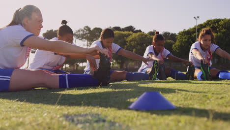 female soccer players sitting on the ground and touching toes on soccer field. 4k