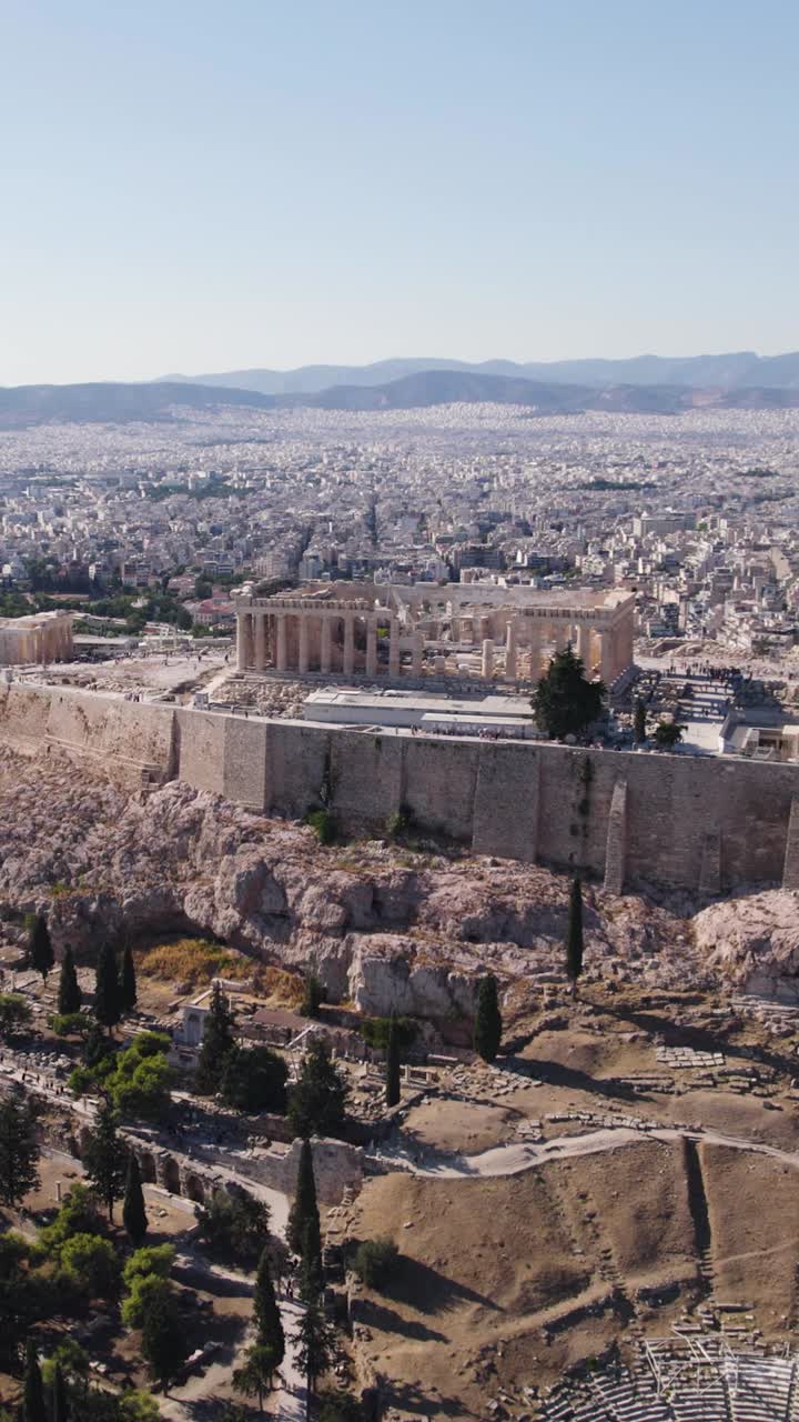 Acropolis and Parthenon standing above Athens cityscape under clear blue sky. Aerial, Circle Dolly, Vertical Video