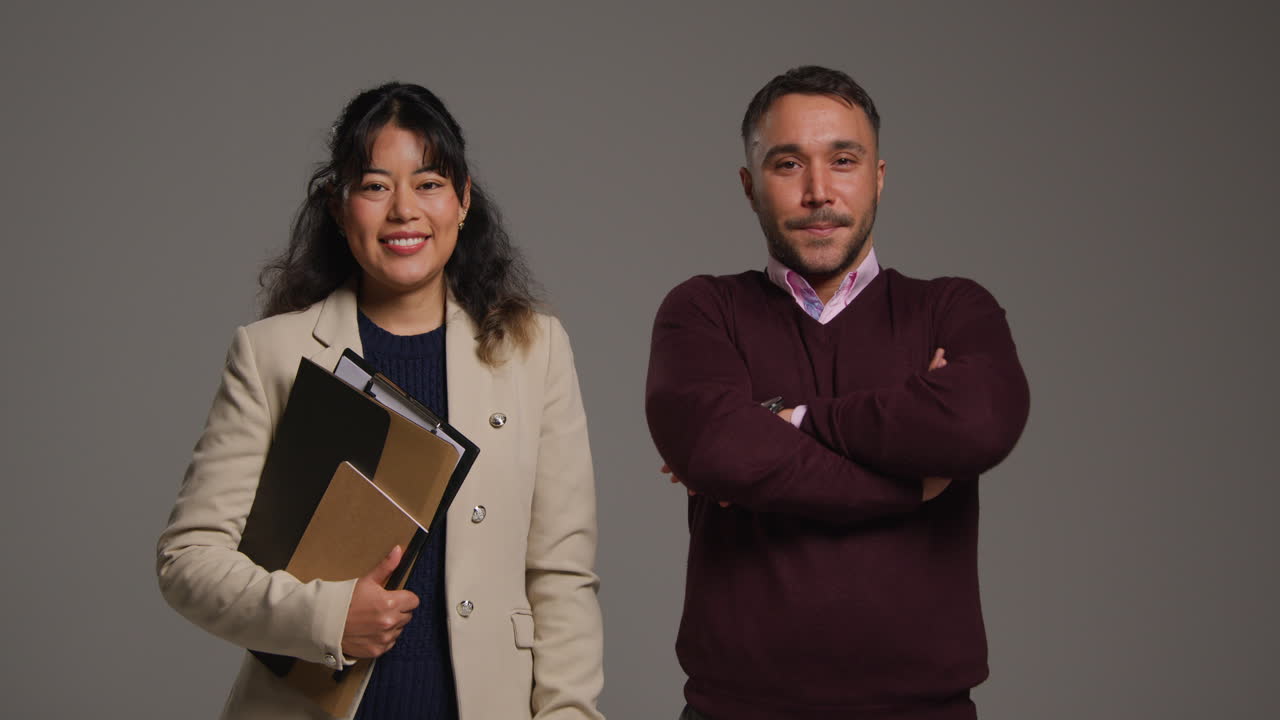 retrato de estudio de maestros y maestras sonrientes sosteniendo una carpeta y cruzando los brazos contra un fondo gris
