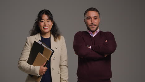 retrato de estudio de maestros y maestras sonrientes sosteniendo una carpeta y cruzando los brazos contra un fondo gris