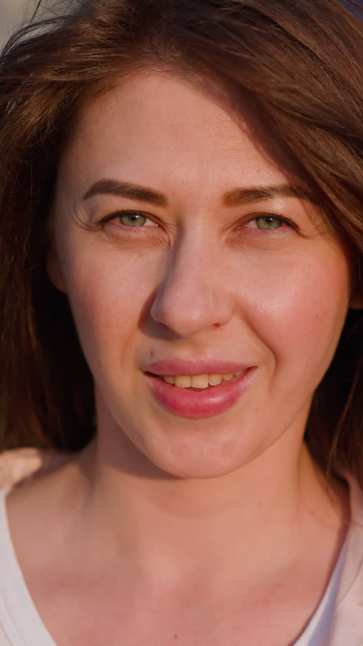 Pretty redhead woman smiles to camera standing on city street closeup slow motion. Attractive lady at sunset light. Cheerful female model
