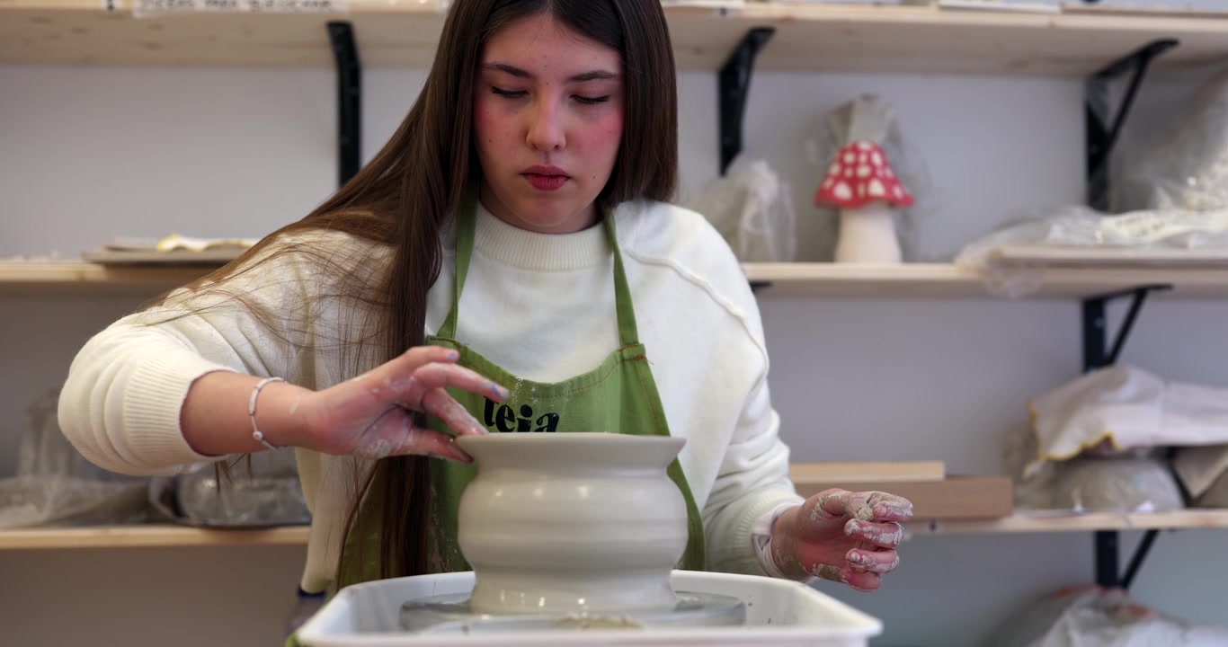Giovane donna che modella un vaso di argilla al tornio da vasaio in uno studio.