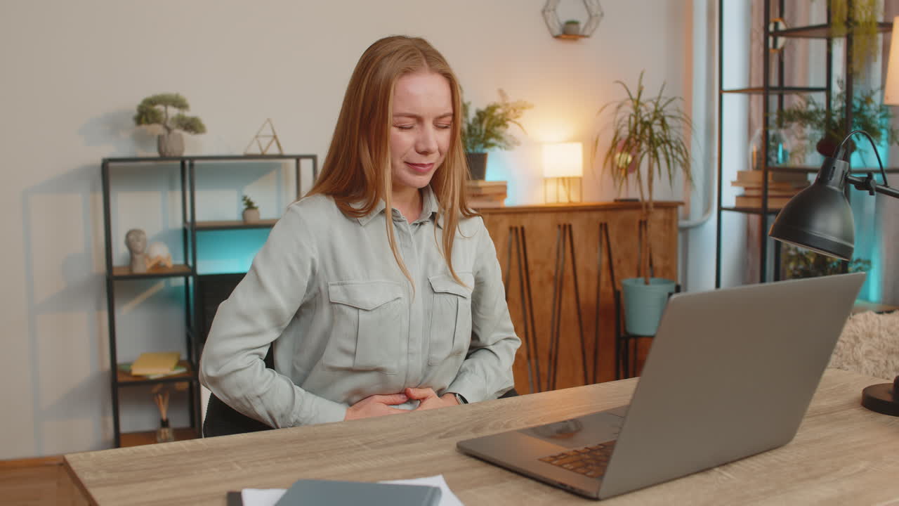 Enttäuschte Frau mittleren Alters fühlt sich nach übermäßigem Essen während der Arbeit am Laptop im Home-Office.